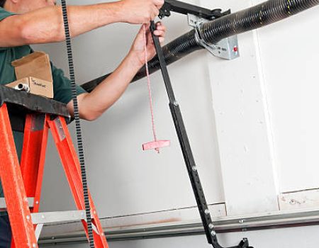 A worker is replacing the traveler car on a belt driven garage door opener.