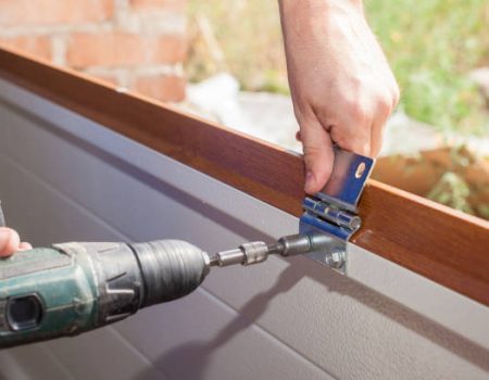 Fixing and replacement concept. Cropped view of professional worker using electric screwdriver and install new garage door system in house under construction